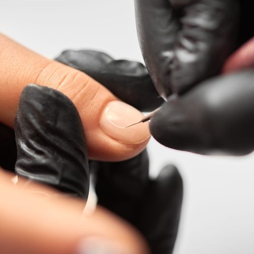 Process of making fashionable manicure in beauty salon. Close-up of professional master manicurist hands painting patterns on client woman nails using applicator on light blurred background.